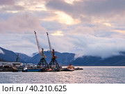 Вид на бухту Провидения, краны морского порта и горы, покрытые облаками. Утрений пейзаж. Восхода солнца над морской бухтой. Портовый посёлок в Арктике. Провидения, Чукотка, Дальний Восток России. Стоковое фото, фотограф Андрей Степанов / Фотобанк Лори