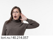 Portrait of intrigued and curious funny young woman eavesdropping on someone's interesting conversation.Surprised girl with her mouth open listens with her hand to her ear.Copy Space.White background. Стоковое фото, фотограф Регина Ерофеева / Фотобанк Лори
