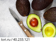 Whole and cut in half ripe organic avocados and a knife on a grey  background. The Haas Avocado. Source of vitamins , trace elements , beta-carotene and omega-3 fatty acids . Healthy food, diet. Стоковое фото, фотограф Виктория Панченко / Фотобанк Лори