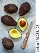 Whole and cut in half ripe organic avocados and a knife on a grey  background. The Haas Avocado. Source of vitamins , trace elements , beta-carotene and omega-3 fatty acids . Healthy food, diet. Стоковое фото, фотограф Виктория Панченко / Фотобанк Лори