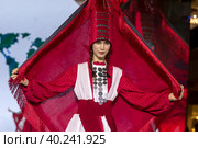 Женщина демонстрирует Удмутрский национальный костюм на подиуме в рамках шоу "Грани Мира" на фестивале детской моды Kids Fashion Week в "Центральном детском магазине на Лубянке" (ЦДМ) в Москве, Россия (2023 год). Редакционное фото, фотограф Николай Винокуров / Фотобанк Лори