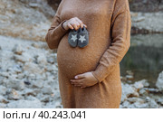 Pregnant woman in a brown sweater with booties in her hands close-up, body parts, on the background of the beach, the concept of waiting for a child, parents, parenting and caring for a newborn. Стоковое фото, фотограф Ирина Компаниец / Фотобанк Лори