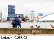 Minsk, Belarus - January 07, 2019: Mother and child on the banks of the river. Waterfront, birds. Редакционное фото, фотограф Denis Shitikoff / Фотобанк Лори