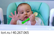 A hungry baby is gnawing on a plastic spoon at the table on a high chair. Teething, whims, itchy gums, introduction of complementary foods. Стоковое видео, видеограф Ольга Симонова / Фотобанк Лори