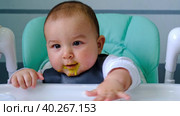 A hungry baby taps his hand on the table on a high chair, asks to eat, nibbles on a spoon. Teething, whims, itchy gums, introduction of complementary foods. Стоковое видео, видеограф Ольга Симонова / Фотобанк Лори