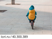 A cheerful little boy rides a bicycle outdoors. A happy child walks in the spring park. The baby is dressed in a fashionable yellow vest and turquoise jumpsuit. Стоковое фото, фотограф Photojuli / Фотобанк Лори