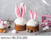 Beautiful stylish still life. Easter cake with rabbit (hare) ears, meringue, marshmallows, Easter eggs and willow branches and on a light concrete background. Happy Easter. Стоковое фото, фотограф Photojuli / Фотобанк Лори