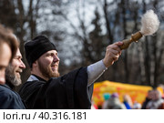Russia, the City of Vidnoye, April 15, 2023. Easter service. The priest sprinkles people and Easter treats with holy water at the entrance to the temple. People go to sanctify eggs and cakes. Редакционное фото, фотограф Photojuli / Фотобанк Лори