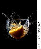 A piece of lemon and orange falls into a glass of water and splashes fly in all directions. Стоковое AI-изображение, AI-художник Ярославский Максим / Фотобанк Лори