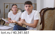 Upset young wife, holding documents in her hands, swears at her husband in the apartment and expresses her dissatisfaction. Стоковое видео, видеограф Яков Филимонов / Фотобанк Лори
