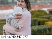 A young mother holds a charming little son in her arms. The kid looks at the camera and smiles. Portrait of a beautiful chubby 4-month-old baby. Стоковое фото, фотограф Photojuli / Фотобанк Лори