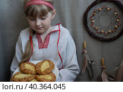 Светловолосая девочка в русском народном костюме держит тарелку с карельскими калитками и смотрит на них (2023 год). Стоковое фото, фотограф Наталья Зверева / Фотобанк Лори