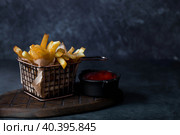 French fries in a metal basket with salt and ketchup on a stylish board on a dark background. Fried potatoes. The concept of fast food and junk food. Стоковое фото, фотограф Photojuli / Фотобанк Лори