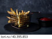 French fries in a metal basket with salt and ketchup on a stylish board on a dark background. Fried potatoes. The concept of fast food and junk food. Стоковое фото, фотограф Photojuli / Фотобанк Лори