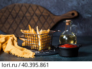 French fries in a metal basket with salt, ketchup and sunflower oil on a stylish board on a dark background. Fried potatoes. The concept of fast food and junk food. Стоковое фото, фотограф Photojuli / Фотобанк Лори