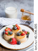 Cottage cheese pancakes, Russian cheesecakes with fresh blueberries, strawberries, honey and mint leaves on a stylish wooden board on a gray concrete table. Natural products. Healthy and delicious breakfast. Стоковое фото, фотограф Photojuli / Фотобанк Лори
