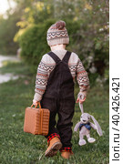 A little boy of 4 years old outdoors with a suitcase and a stuffed rabbit goes on a journey. A beautiful portrait of a child playing on the street. Стоковое фото, фотограф Photojuli / Фотобанк Лори
