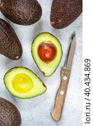 Whole and cut in half ripe organic avocados and a knife on a grey background. The Haas Avocado. Source of vitamins , trace elements , beta-carotene and omega-3 fatty acids . Healthy food, diet. Стоковое фото, фотограф Виктория Панченко / Фотобанк Лори