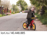 A cheerful little boy rides a bicycle outdoors. A happy child walks in the spring park. The baby is dressed in a fashionable vest, overalls. An aviator's hat is on his head. Стоковое фото, фотограф Photojuli / Фотобанк Лори