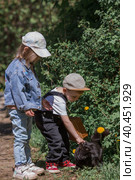 A little girl and a boy in stylish clothes play with a black cat outdoors. The concept of pet care. Children and animals. Стоковое фото, фотограф Photojuli / Фотобанк Лори