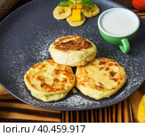 Syrniki or cheese pancakes with cream sauce and bananas on a plate on wooden table close up. Стоковое фото, фотограф Татьяна Терехина / Фотобанк Лори