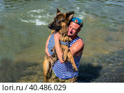 Moscow, Russia - August 02, 2017: Russian paratrooper holds a large dog in the vest in his arms. Редакционное фото, фотограф Iva Noel / Фотобанк Лори