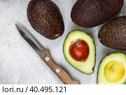 Whole and cut in half ripe organic avocados and a knife on a grey background. The Haas Avocado. Source of vitamins , trace elements , beta-carotene and omega-3 fatty acids . Healthy food, diet. Стоковое фото, фотограф Виктория Панченко / Фотобанк Лори