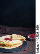 Pile or stack of russian homemade traditional blinis or thin pancakes with red berries served on round stone tray ready for eating on dark brown wooden table. Image with copy space, vertical. Стоковое фото, фотограф Елена Кабенкина / Фотобанк Лори
