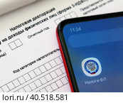 Телефон с электронным приложением налоговой службы "Налоги ФЛ" лежит на бланке налоговой декларации 3-НДФЛ. Оформление социального и имущественного вычета через интернет (2023 год). Редакционное фото, фотограф Татьяна Т / Фотобанк Лори