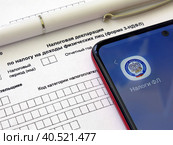 Телефон с электронным приложением налоговой службы "Налоги ФЛ" лежит на бланке налоговой декларации 3-НДФЛ. Оформление социального и имущественного вычета через интернет (2023 год). Редакционное фото, фотограф Татьяна Т / Фотобанк Лори