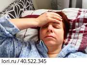 Sick woman in bed. Headache, runny nose and cold. Paleness of the face and faintness of the body. Feeling unwell. The patient holds his forehead with his hand and covers his eyes. Стоковое фото, фотограф Юлия Петровская / Фотобанк Лори