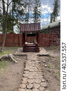 Antique wooden water well. Old wooden well.Old wooden wheel and bucket of water inside on grass ground, primitive knowhow. "Partisan village". Military-patriotic park "Patriot", Kubinka stock photo. Редакционное фото, фотограф Екатерина Казначеева / Фотобанк Лори