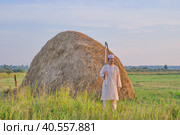 An senior Muslim man in a skullcap and traditional clothes leaves with a hand scythe from the hay field at sunset. Стоковое фото, фотограф Ирина Кононова / Фотобанк Лори
