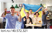 Excited adult young supporters with flag of Ukraine, rejoicing victory with beer and snacks in pub. Стоковое видео, видеограф Яков Филимонов / Фотобанк Лори