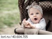 Funny bored baby with blue eyes sitting in stroller, sad looking at camera. Adorable pensive cute child infant yawns wide open mouth in pram. Concept of infancy, childhood emotion. Copy ad text space. Стоковое фото, фотограф Aleksandr Golubev / Фотобанк Лори