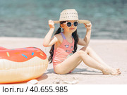 Cute little girl sitting on the sand on a beach in a swimsuit and straw hat. Стоковое фото, фотограф Ирина Михайличенко / Фотобанк Лори
