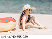 Side view of cute little girl sitting on the sand on a beach in a swimsuit and straw hat. Стоковое фото, фотограф Ирина Михайличенко / Фотобанк Лори