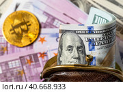 Толстая пачка сто-долларовых купюр лежит в старом, потертом кошельке на фоне купюр европейской валюты евро и монеты биткоин. Стоковое фото, фотограф Николай Винокуров / Фотобанк Лори