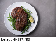 Стейк Рибай с рукколой на белой тарелке с лаймом на сером фоне, вид сверху. Ribeye steak with arugula on a white plate with lime on a grey background, top view. Стоковое фото, фотограф Максим Коломыченко / Фотобанк Лори