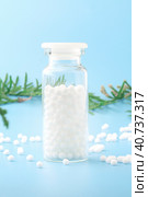 Homeopathic globules and glass bottle near with fresh juniper branches close-up on blue background. Alternative Homeopathy medicine herbs.Vertical. Copy space. Стоковое фото, фотограф Tatiana Syrtseva / Фотобанк Лори