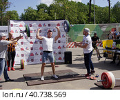Молодой мужчина выжимает штангу на спортивном празднике. Два тренера страхуют по бокам. (2019 год). Редакционное фото, фотограф Сергей Никифоров-Гордеев / Фотобанк Лори