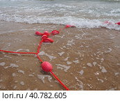 Buoys on a rope in sea water. The lifebuoys are pink restraints to alert people to the depth of the water. Rescue of the drowning. Delimiting a place on sandy beach between hotels. Wave with bubbles. Стоковое фото, фотограф Юлия Петровская / Фотобанк Лори