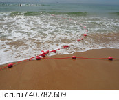 Buoys on a rope in sea water. The lifebuoys are pink restraints to alert people to the depth of the water. Rescue of the drowning. Delimiting a place on sandy beach between hotels. Wave with bubbles. Стоковое фото, фотограф Юлия Петровская / Фотобанк Лори