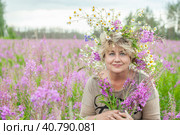 Beautiful 60s mid mature woman at nature in a a wreath of flowers in hair. Gorgeous looking old happy lady smiling. Summertime vibe. Peace and harmony. Healthy skin care. Стоковое фото, фотограф Оксана Медведева / Фотобанк Лори