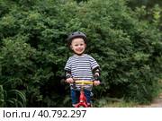 A cheerful little boy rides a running bike in a helmet outdoors. A happy child is engaged in an active sport. Protection. Life insurance and child safety. Стоковое фото, фотограф Photojuli / Фотобанк Лори