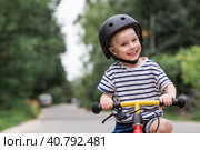A cheerful little boy rides a running bike in a helmet outdoors. A happy child is engaged in an active sport. Protection. Life insurance and child safety. Стоковое фото, фотограф Photojuli / Фотобанк Лори