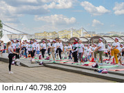 Пенсионеры, участники спортивного праздника программы "Московское долголетие", в фирменных московских футболках и шапочках, стоя на разноцветных гимнастических ковриках, выполняют гимнастику под руководством опытного тренера в парке Музеон на фоне Крымского моста и голубого неба с красивыми белыми облаками (2023 год). Редакционное фото, фотограф Сергей Никифоров-Гордеев / Фотобанк Лори