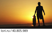 Black silhouette of a man standing near the ocean holding a longboard at bright orange sunset. Стоковое видео, видеограф Константин Шишкин / Фотобанк Лори