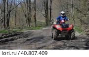A red quad bike with a girl behind the wheel is about to drive through a puddle in the spring woods. Front view. Extreme type of outdoor activities. ATV riding. Стоковое фото, фотограф Воловодов Владимир / Фотобанк Лори