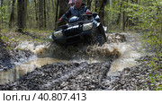A couple on a black ATV riding through a muddy puddle in the woods. Front view. Extreme type of outdoor activities. Riding on a quad bike. Стоковое фото, фотограф Воловодов Владимир / Фотобанк Лори
